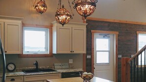 A kitchen with a central island, pendant lighting, and a view of the outdoors through a window. -  30 Mins to Waterton Gate! Relax & Enjoy the View of Chief Mountain & Sunsets (CARDSTON)