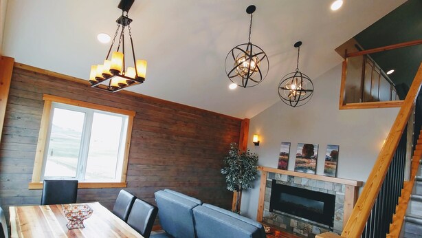 A modern living room with a wooden dining table, blue sofa, and a fireplace. -  30 Mins to Waterton Gate! Relax & Enjoy the View of Chief Mountain & Sunsets (CARDSTON)