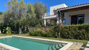 Ein rechteckiger Pool mit Steinplatten, umgeben von einer Steindeck, mit einem weißen Gebäude mit Balkon im Hintergrund.