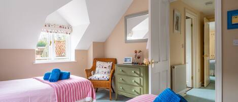 A bedroom with two beds, a chair, a dresser, and a window.