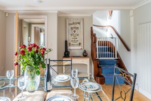 A dining area with a glass table set for six, a vase of red roses, and a staircase with blue carpeting. - The Manse, South Creake, Norfolk (South Creake)