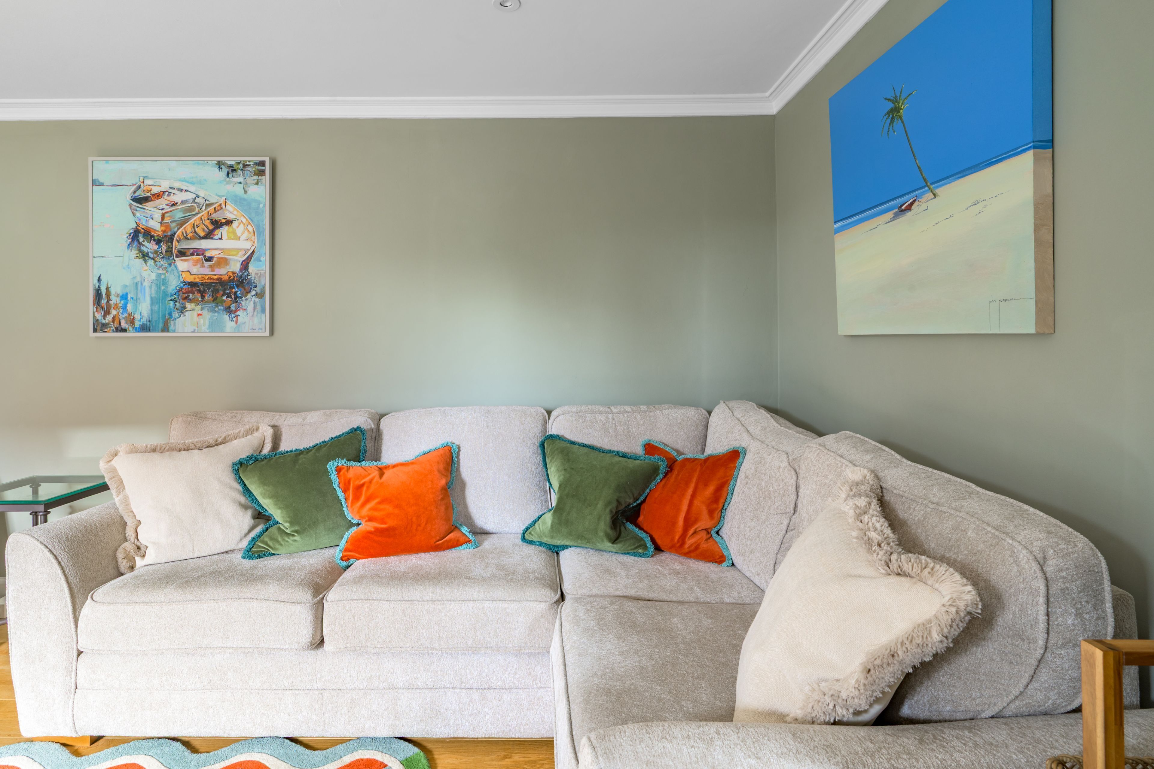 Un salon avec un canapé, des coussins et deux tableaux accrochés au mur.