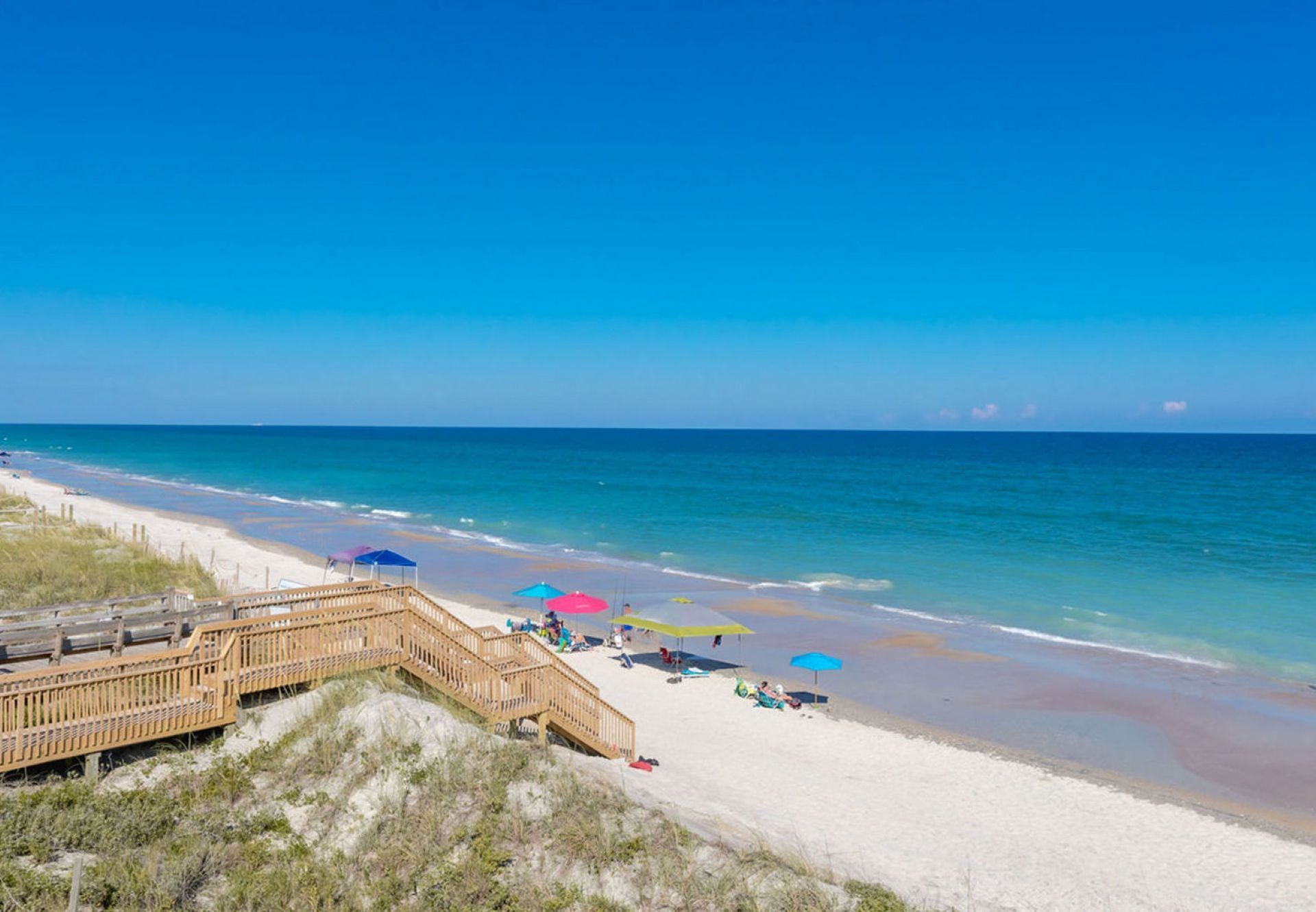 Une plage avec une promenade en bois, des parasols et des gens qui se détendent sur le sable.