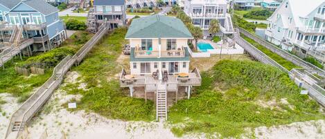 A beachfront property with multiple houses, a central building with a pool, and a wooden boardwalk leading to the beach.