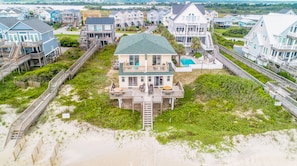 Una propiedad frente a la playa con varias casas, un edificio central con piscina y un paseo marítimo de madera que conduce a la playa.