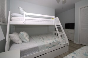 Una cama litera con escalera, un televisor y un aparador en un dormitorio.