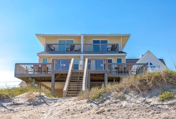 A two-story beachfront house with a balcony and a staircase leading to the upper level.