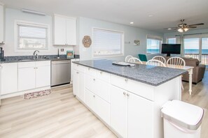 A modern kitchen with white cabinetry, a granite countertop, and a dining area with white chairs.