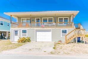 A two-story house with a garage, a balcony, and a staircase leading to an upper level. - 75 Trips - 3BR 2nd Row Home - Covered Porch & Bonus Space; Dog Friendly! (Topsail Beach)