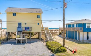 Situated near the beach, this two-story building offers a small porch area with a bench and a signboard.