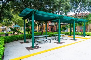 Un espacio al aire libre con techo, mesas de picnic y juegos infantiles.