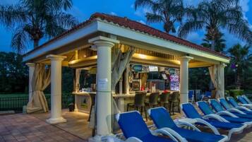 A covered outdoor seating area with blue lounge chairs and a bar.
