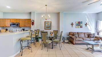 A spacious living area with a dining table, chairs, a sofa, and a kitchen area with wooden cabinets and appliances.