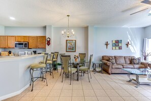A spacious living area with a dining table, chairs, a sofa, and a kitchen area with wooden cabinets and appliances.