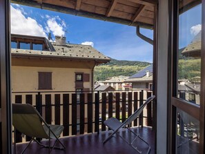 Un balcón con vistas a un paisaje montañoso, una valla de madera y una silla.