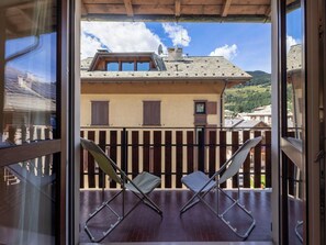 A balcony with two chairs and a view of a building with a tiled roof.