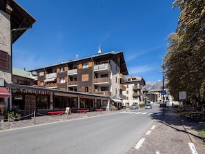 Eine Straße mit mehrstöckigen Gebäuden, Außenbestuhlung und blauem Himmel.