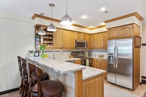A kitchen with wooden cabinets, stainless steel appliances, a marble island, and pendant lighting. - SKI N SKI OUT. 5 Min Walk to Historic Main St.  Ski, Hike, Bike,  out the door. (Park City)