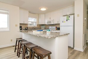 Una cocina con una isla central, taburetes de bar, armarios blancos, un microondas y un refrigerador.