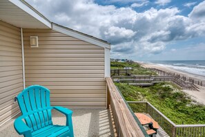 A balcony with a view of the beach, a turquoise chair, and a wooden deck.