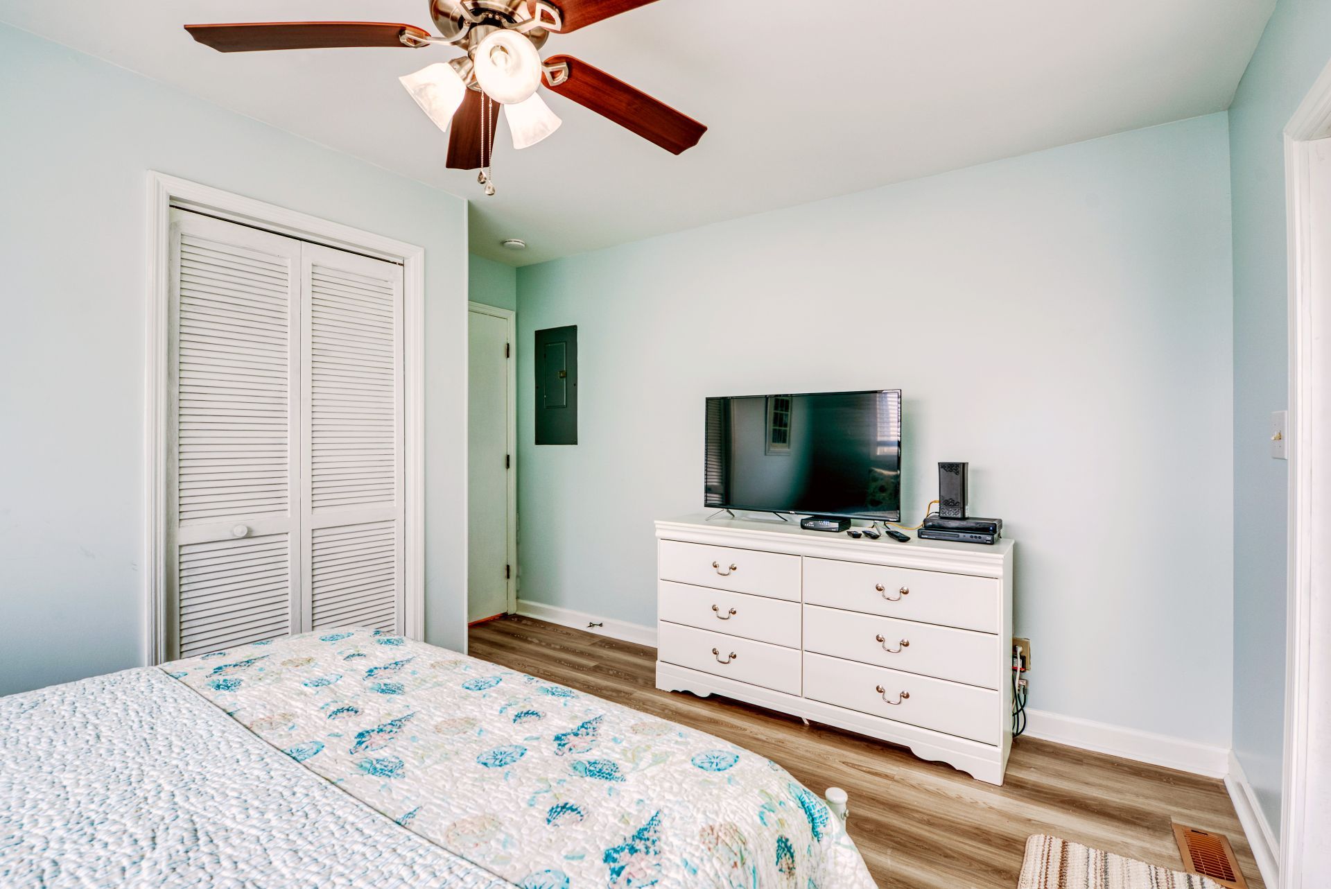 A bedroom with a bed, a dresser, a television, and a ceiling fan.