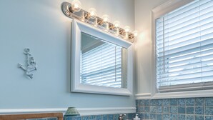 Een badkamer met een houten wastafelmeubel, een spiegel met verlichting en blauwe betegelde wanden.