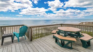 Een houten terras met een picknicktafel en stoelen, met uitzicht op het strand.