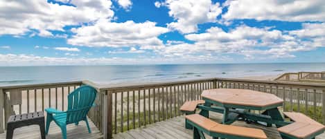 A wooden deck with a picnic table and chairs overlooking a beach.
