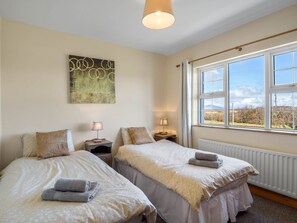 A bedroom with two beds, a radiator, a window with a view, and a painting on the wall.