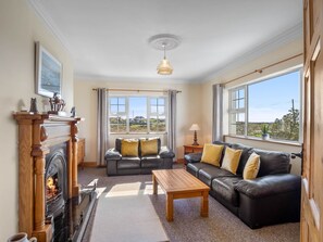 A living room with a fireplace, leather sofas, a wooden coffee table, and large windows offering a view.