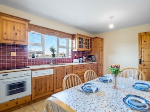 A kitchen with wooden cabinets, a dining table set with blue plates, and a window with a view.