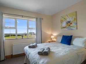 A hotel room with a bed, a window with curtains, a radiator, a lamp, and a painting on the wall. - Annerfield House (Ballyconneely)