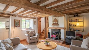 A cozy living room with exposed wooden beams, a fireplace, a sofa, a coffee table, and a bookshelf. - Little Wells (4), North Creake, Norfolk (Fakenham)