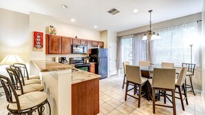 A kitchen with a central island, wooden cabinets, and a dining area with chairs and a table.
