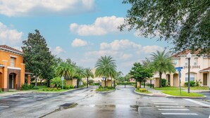 A residential street with houses, palm trees, and a gated entrance.