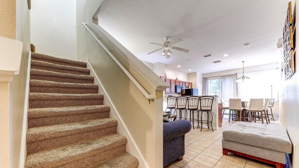 A staircase leading to a living area with a ceiling fan, a dining table with chairs, and a sofa.