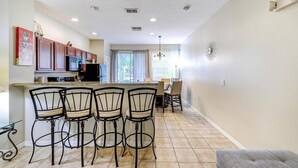 A kitchen with a dining area, featuring a bar with four chairs, a microwave, and a refrigerator.