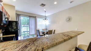 A kitchen with a granite countertop, a dining area with chairs, a chandelier, and a view of the outdoors.