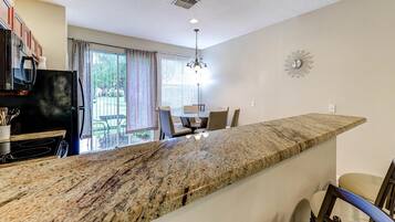A kitchen with a granite countertop, a dining area with chairs, a chandelier, and a view of the outdoors.
