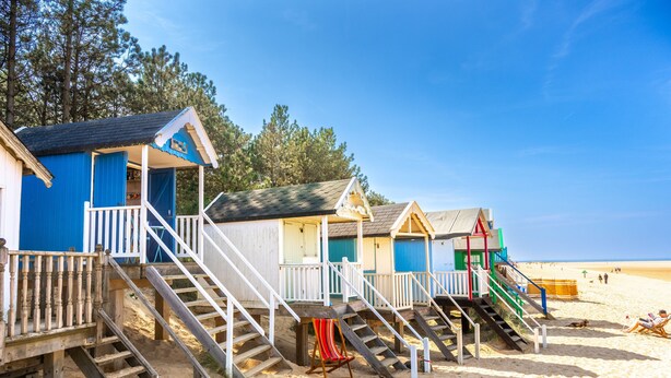 A row of beach huts with wooden stairs leading up to them, situated on a sandy beach with clear skies. - Holly Cottage, Wells-next-the-Sea, Norfolk (Wells-Next-The-Sea)
