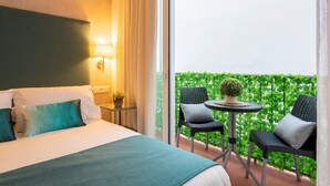 Ein Hotelzimmer mit Bett, Nachttisch, Lampe und Blick auf einen mit Grünpflanzen bewachsenen Balkon.