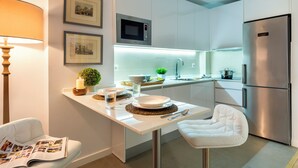 Eine moderne Küche mit weißen Schränken, einer eingebauten Mikrowelle, einem Edelstahlkühlschrank und einem Essbereich mit weißem Tisch und Stühlen.