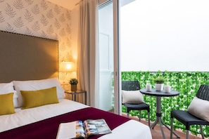 A hotel room with a bed, a bedside table with a lamp, a magazine, and a balcony with a table and chairs.