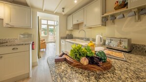 A kitchen with white cabinets, a granite countertop, and a wooden cutting board with vegetables. - Sutton Cottage, Thornham, Norfolk (Thornham)