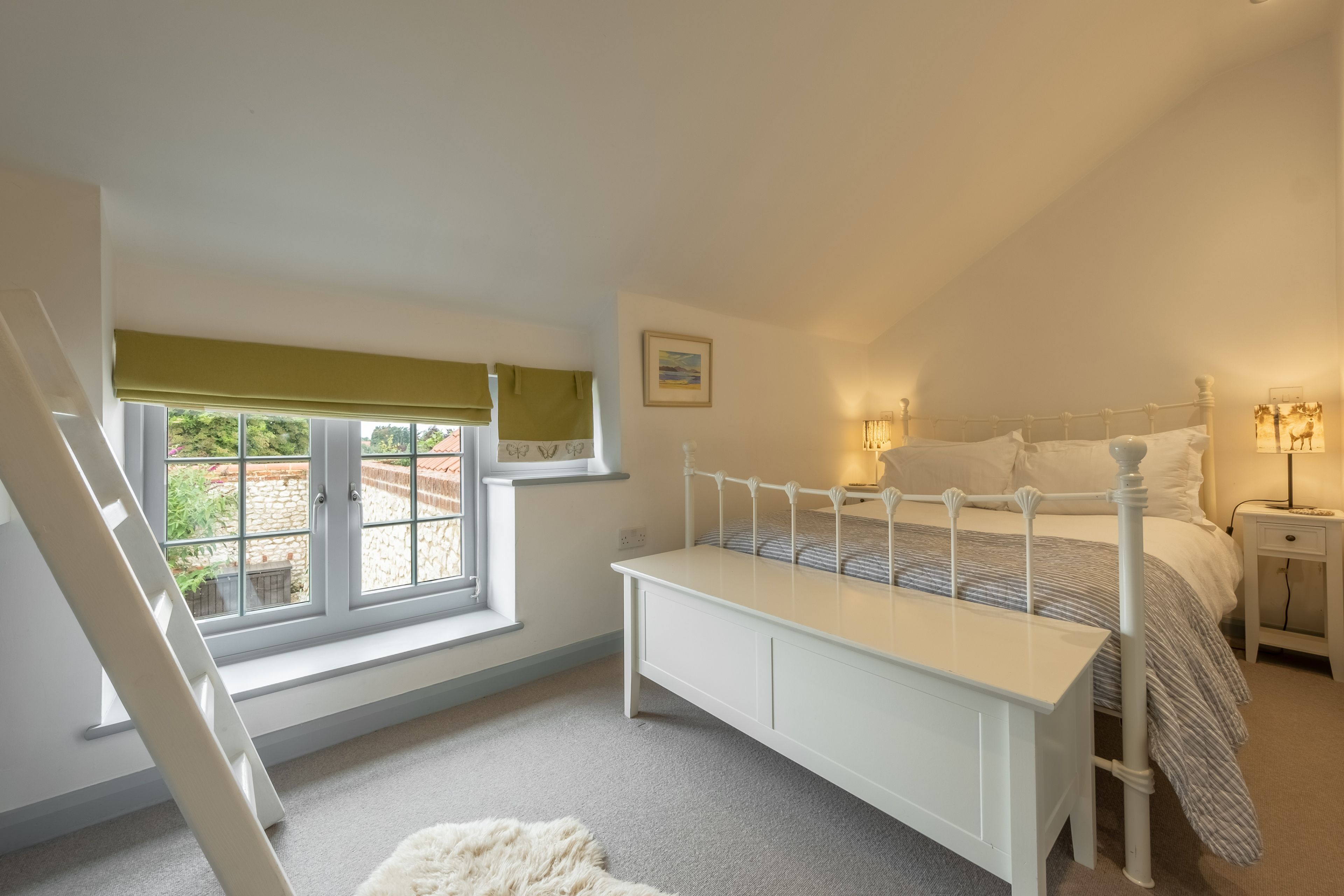 A bedroom with a white bed, bedside tables, a window with a view, and a ladder.