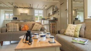 A cozy living room with a wooden coffee table, a sofa, and a kitchen in the background. - Sutton Cottage, Thornham, Norfolk (Thornham)