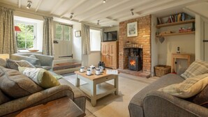 A cozy living room with a fireplace, sofas, and a coffee table. - Sutton Cottage, Thornham, Norfolk (Thornham)