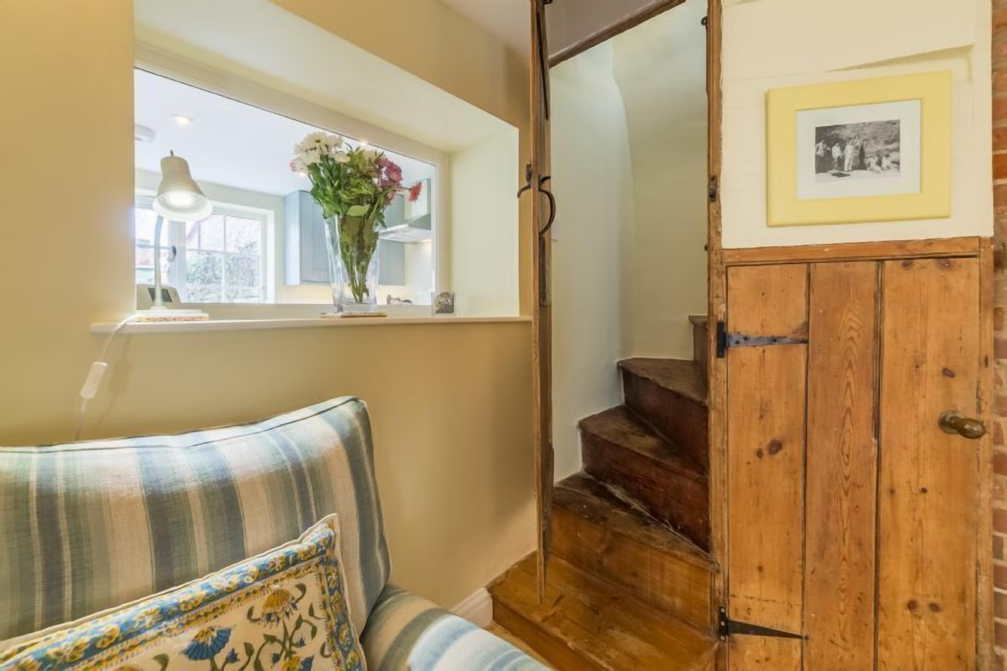 A staircase with a wooden finish, a window with a vase of flowers, and a framed picture on the wall.