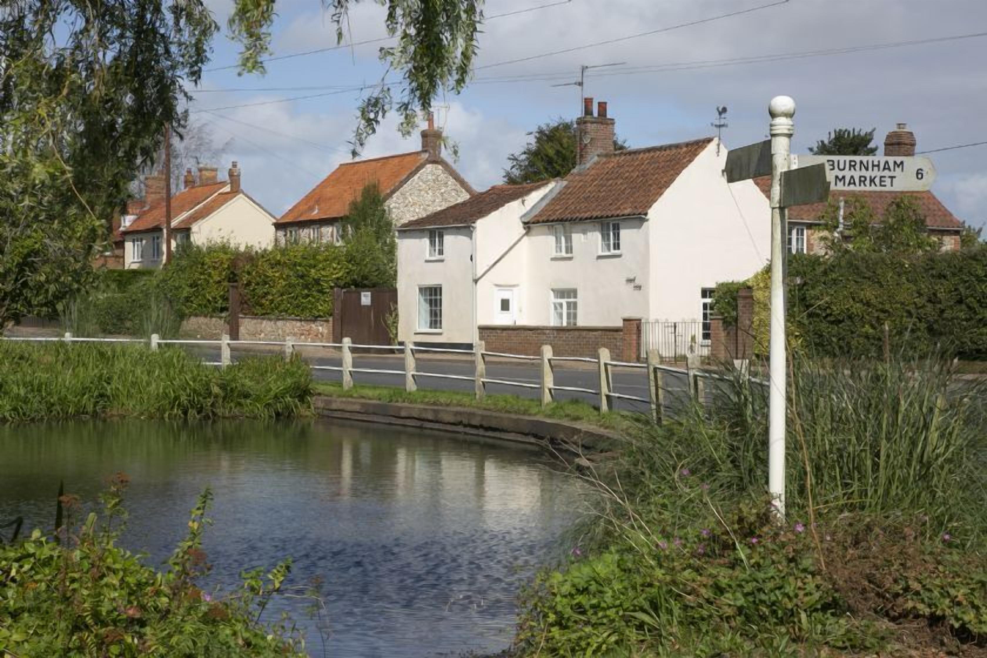 A canal with houses on one side and a signpost indicating Burnham Market 6.