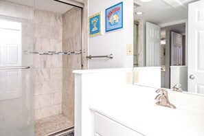 Une salle de bain avec une douche, des toilettes et un lavabo avec un miroir. Deux tableaux encadrés sont accrochés au mur.